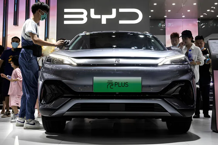 Nell'immagine si vede un'auto di BYD ad un salone con delle persone a fianco che stanno visionando l'auto