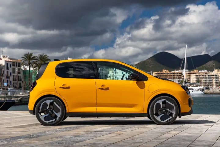 La vista laterale della Renault Twingo 2026 IV E-Tech verniciata in Giallo Mango, cerchi da 18 pollici diamantati e fotografata nel porto di Ibiza