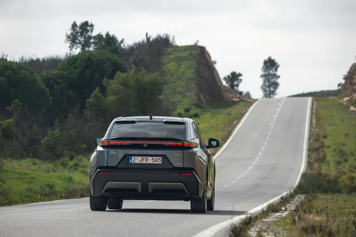 La Toyota C-HR+ 2026 fotografata di posteriore che percorre una strada extraurbana tortuosa e con diversi salsicendi