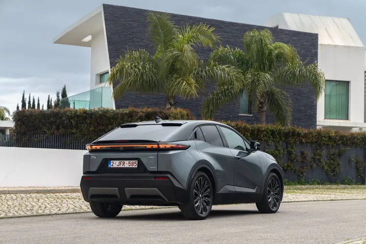 Foto del posteriore della Toyota C-HR+ 2026, posizionata di tre quarti anteriore, con una casa moderna come sfondo