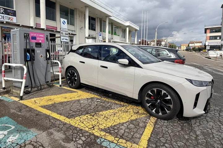 bmw ix alla colonnina di ricarica a roma parcheggiata di lato con al fianco una colonnina di ricarica super fast