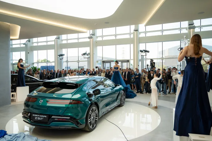 Nell'immagine si vede la presentazione del primo concessionario Denza in Italia a Bologna. Si possono vedere tre musiciste, una direttrice, alcune ballerine di danza moderna, un pubblico numeroso e la Denza Z9 GT nella colorazione Emerald Green