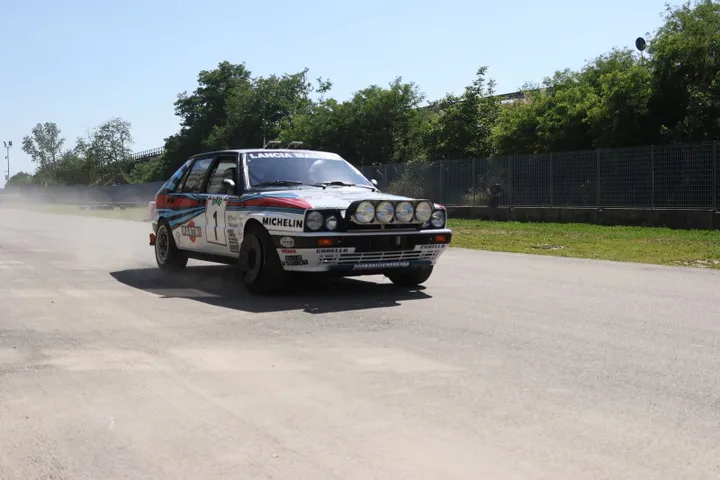 auto da rally lancia a tutta velocità su strada asfaltata con sfondo alberi