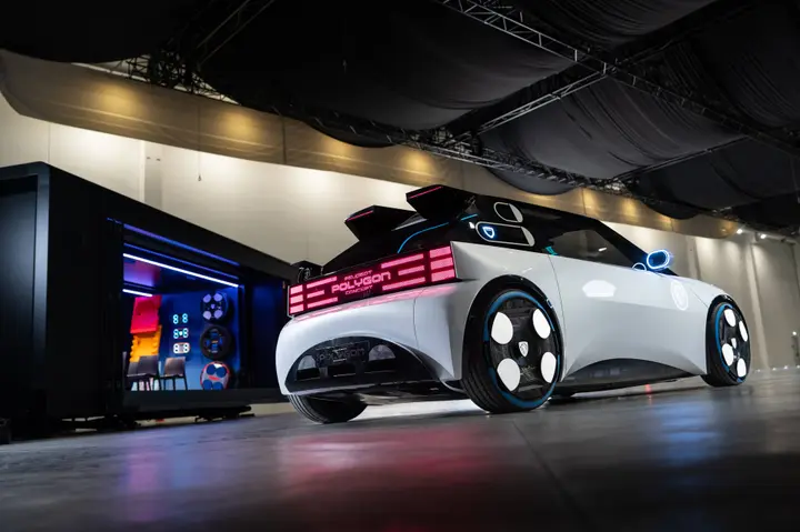 Nell'immagine si vede il retro della Peugeot Polygon e in particolare la striscia di led posteriori che compongono una scritta. Sullo sfondo il prefrabbricato dove si trovano altri volanti e sedili