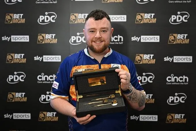 Josh Rock posiert mit den goldenen Pfeilen, die er für seinen Neun-Darter in der Premier League Darts erhielt