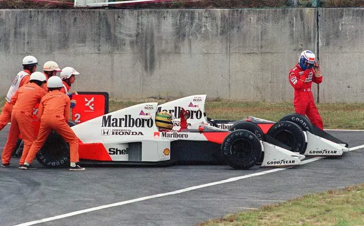 Ayrton Senna of Brazil is given a push from circuit marshals for a restart while his teammate and bitter rival Alain Prost of France leaves his car to abandon the race after the two collided in a chicane during the Japan Formula One Grand Prix in Suzuka 22 October 1989. Senna received the chequered flag but was later disqualified after being accused of receiving an illegal push from marshals and of taking a short cut through the chicane. AFP PHOTO TOSHIFUMI KITAMURA (Photo credit should read TOSHIFUMI KITAMURA/AFP/Getty Images)