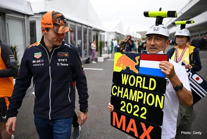 SUZUKA, JAPAN - OCTOBER 06: Max Verstappen of the Netherlands and Oracle Red Bull Racing walks in the Paddock next a fan holding a pit board showing their support during previews ahead of the F1 Grand Prix of Japan at Suzuka International Racing Course on October 06, 2022 in Suzuka, Japan. (Photo by Clive Mason/Getty Images)