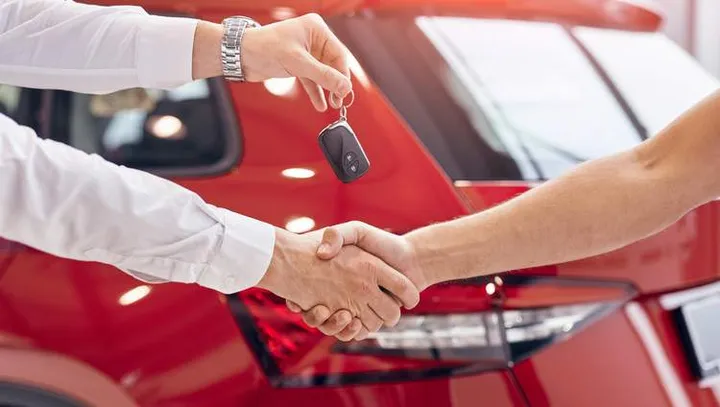 Unrecognizable manager shaking hand of customer and handing keys while sealing deal in car dealership