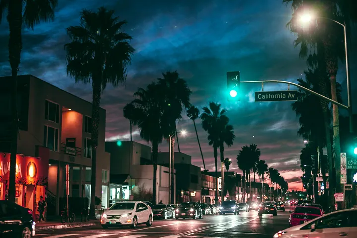Free A bustling night scene featuring cars and palm trees on California Avenue, illuminated by streetlights. Stock Photo