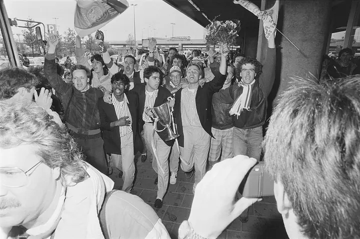Spelers van Ajax met de Europa Cup II-troffee bij aankomst op Schiphol. Op de foto zijn onder meer Aron Winter, Sonny Silooy en Rob Witschge te zien. Foto: Bart Molendijk / Anefo, CC0, via Wikimedia Commons.