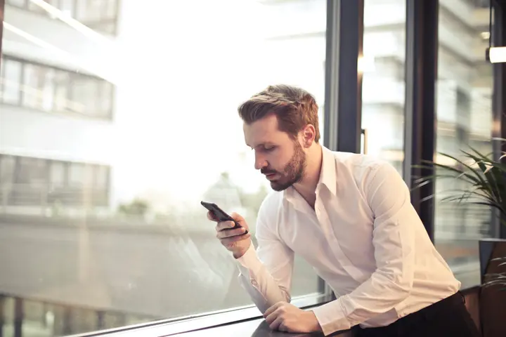photo of man in white dress shirt holding phone near window 859265f1595921456